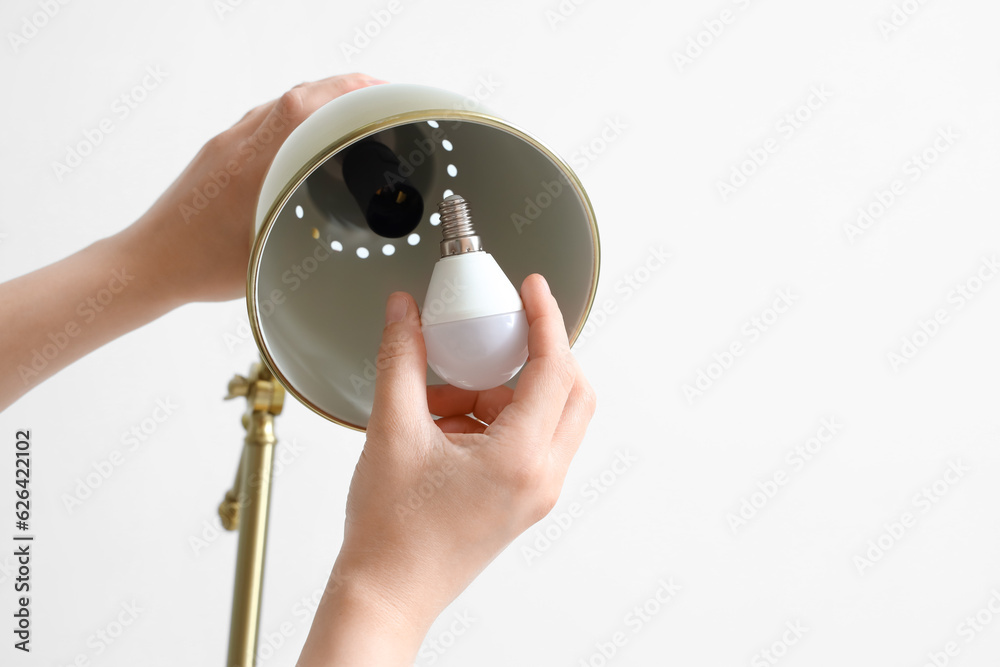 Woman changing light bulb in lamp on light background, closeup