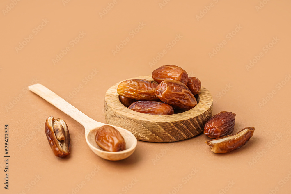 Bowl and spoon with dried dates on brown background