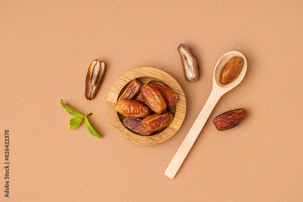 Bowl and spoon with dried dates on brown background