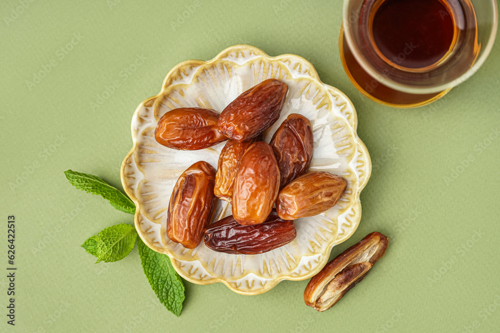 Plate with dried dates and glass of Turkish tea on green background