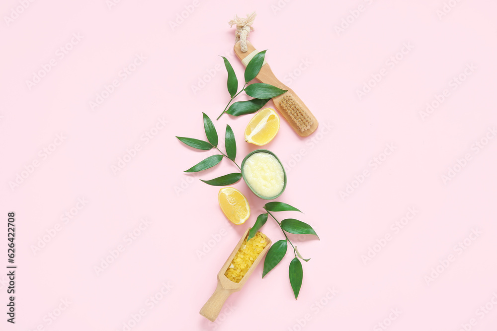 Bowl of lemon body scrub with massage brush and sea salt on pink background