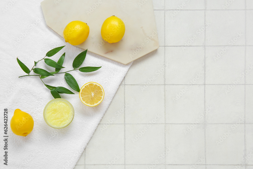 Bowl of lemon body scrub with board and towel on white tile background