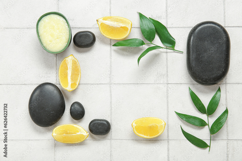 Frame made of lemon body scrub with spa stones and plant branches on white tile background