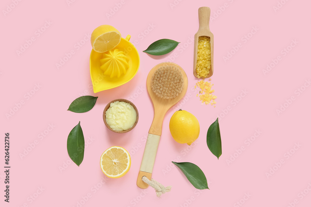 Bowl of lemon body scrub with juicer, sea salt and massage brush on pink background