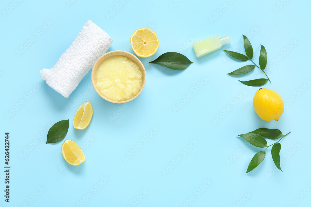 Bowl of lemon body scrub with cosmetic bottle and towel on blue background