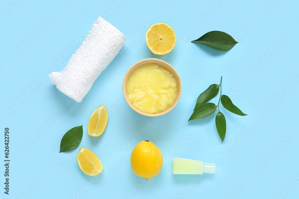 Bowl of lemon body scrub with cosmetic bottle and towel on blue background