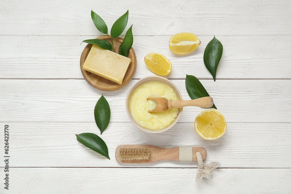 Bowl of lemon body scrub with massage brush and soap on white wooden background