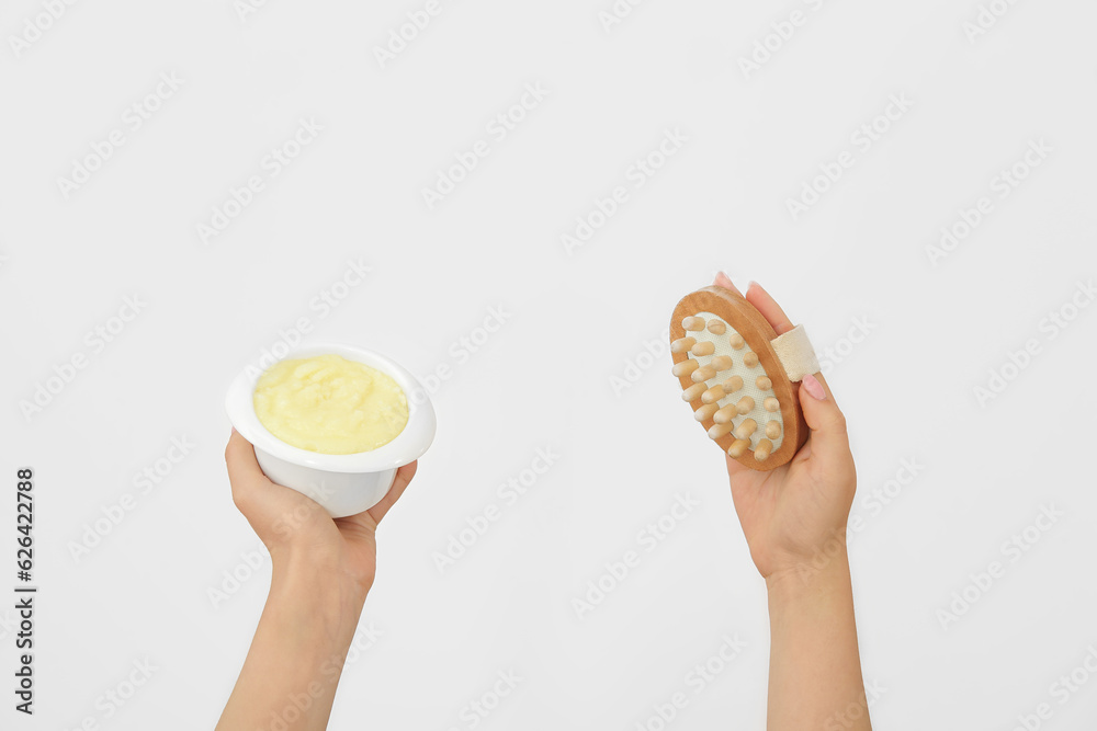 Female hands with bowl of lemon body scrub and massage brush on white background