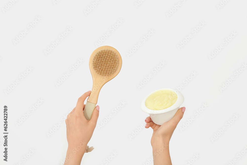 Female hands with bowl of lemon body scrub and massage brush on white background