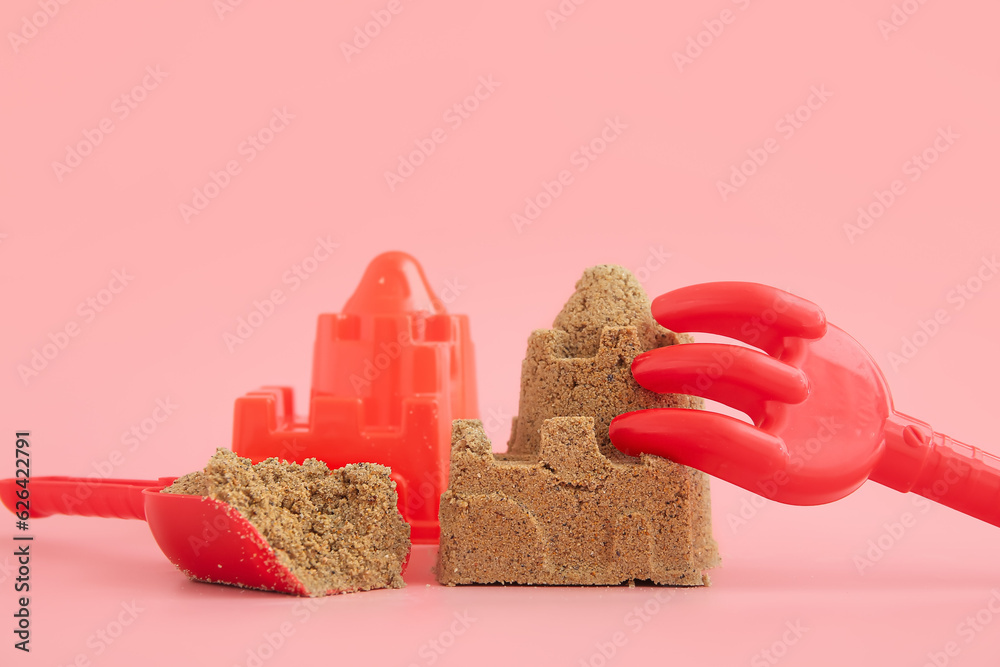 Castle made of sand with beach toys for children on pink background