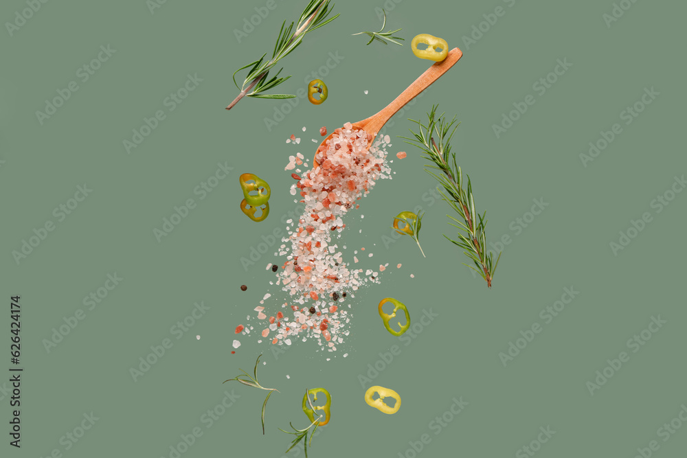 Flying salt, chili pepper and rosemary on green background