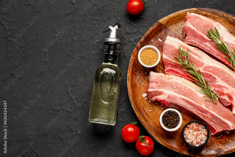 Wooden plate with raw pork ribs, tomatoes, spices and oil on dark background