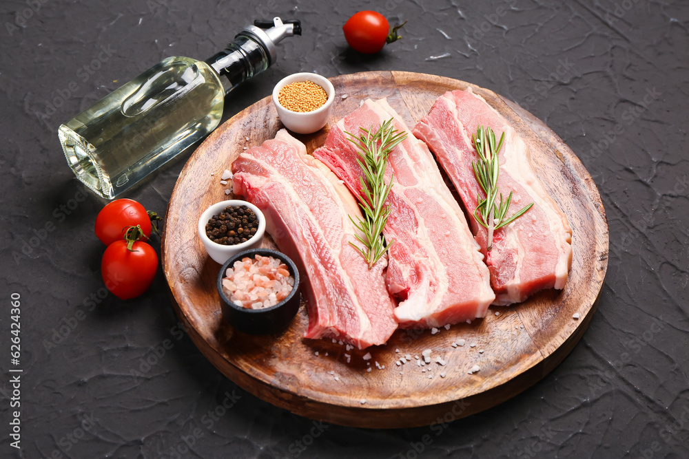 Wooden plate with raw pork ribs, tomatoes, spices and oil on dark background