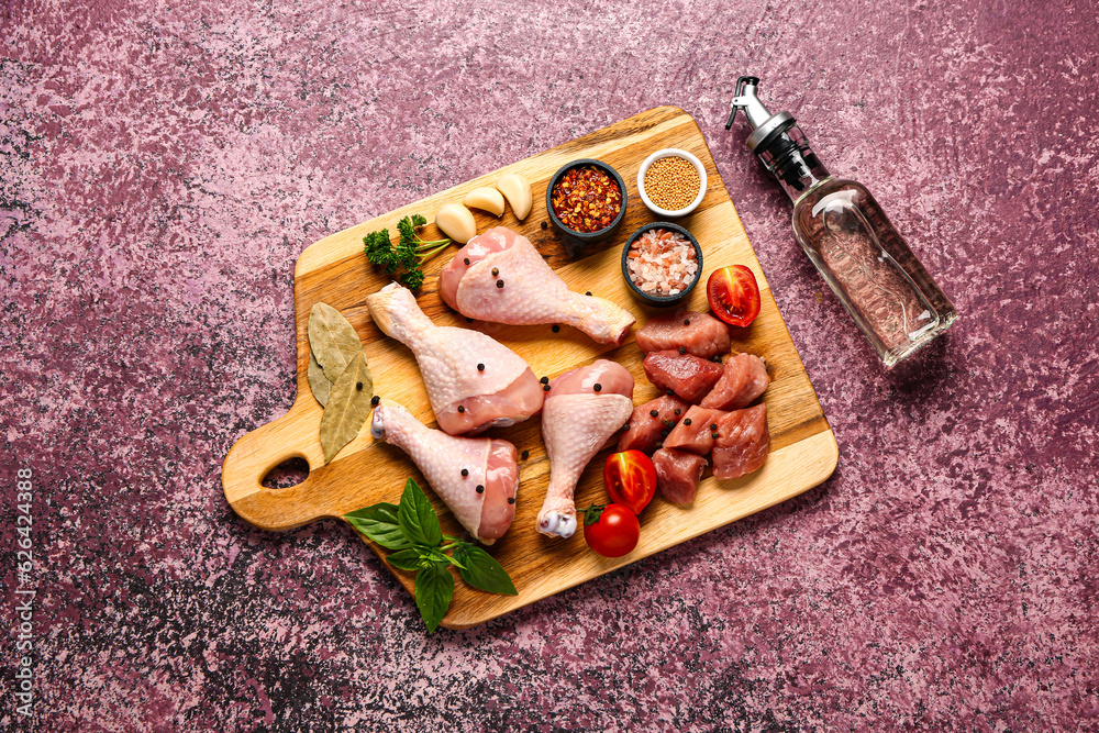 Wooden board with raw meat, spices and oil on color background