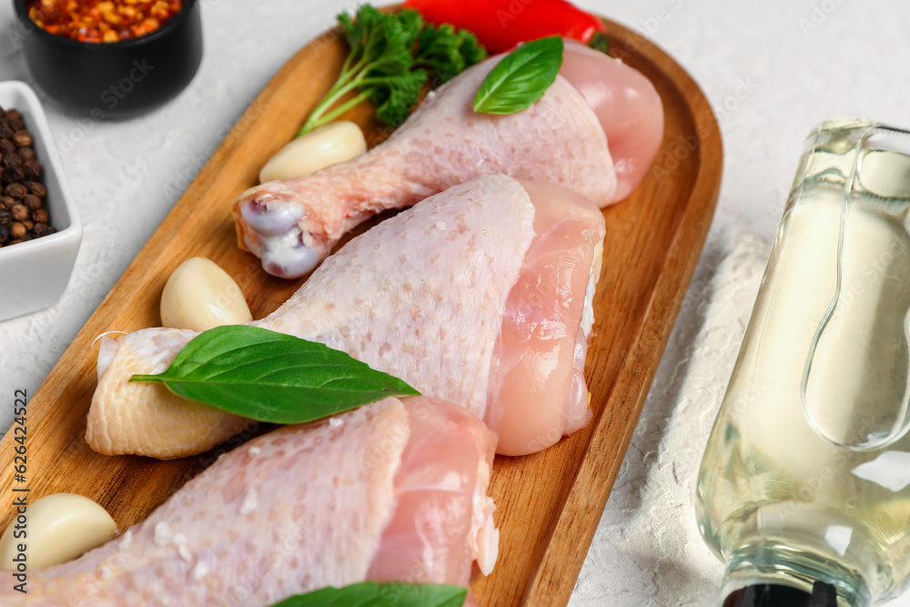 Wooden board with raw chicken legs, garlic, basil and oil on light background, closeup