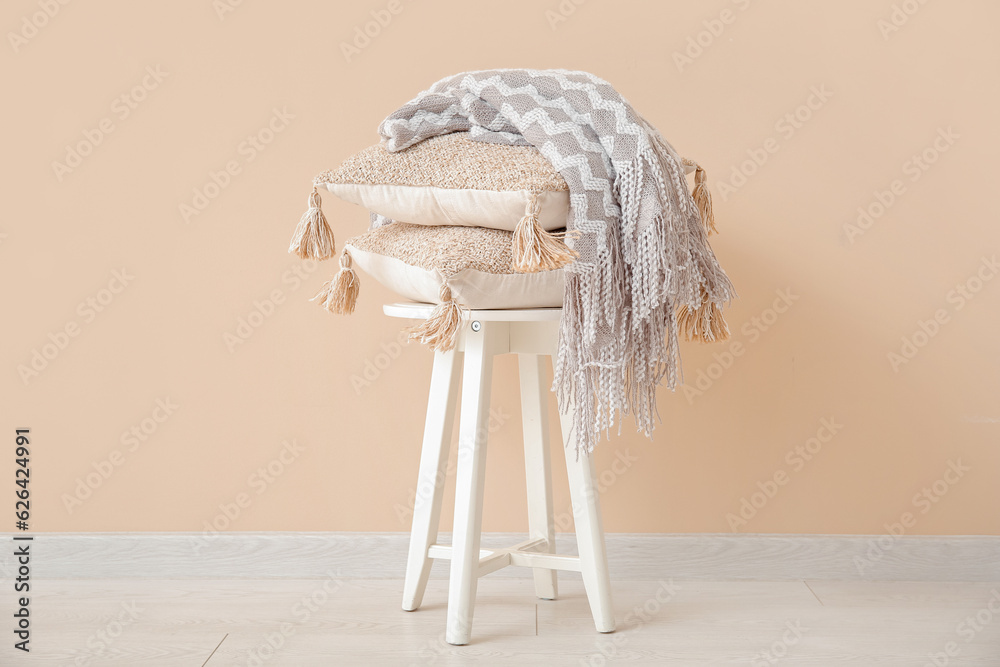 Stool with cozy blanket and cushions near beige wall