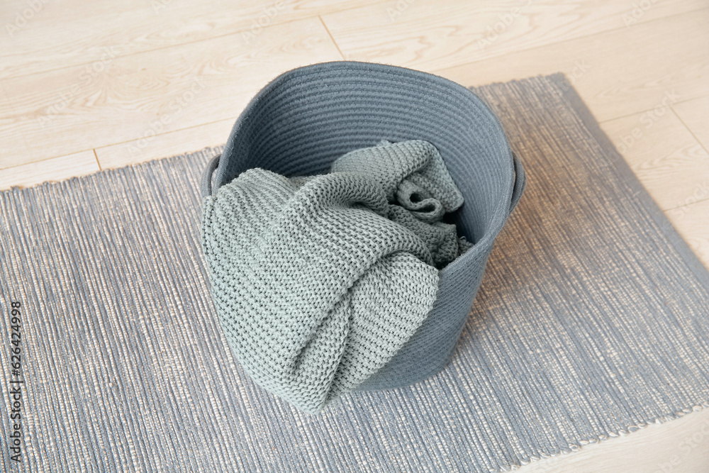 Basket with cozy blanket on floor, closeup