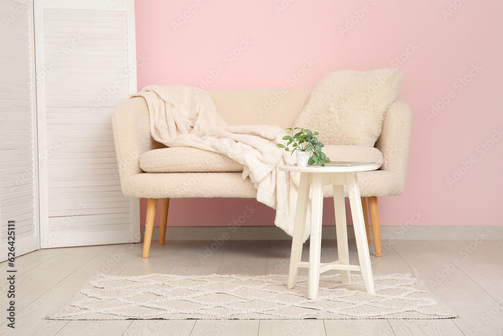 White sofa with cozy blanket near pink wall