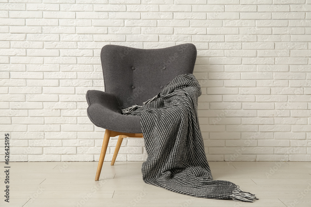 Grey armchair with cozy blanket near white brick wall