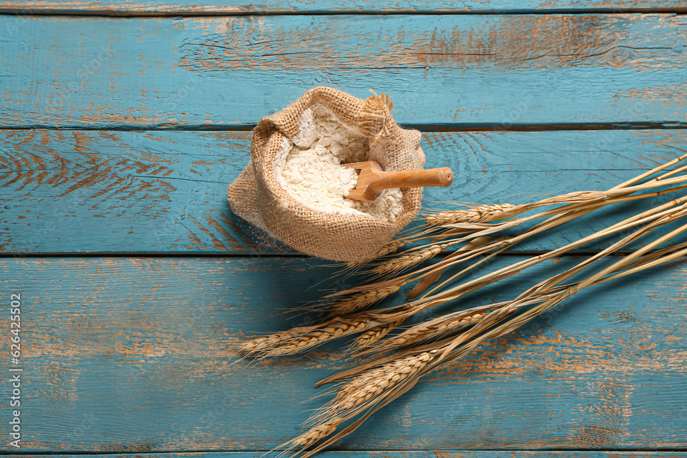 Sack bag with flour and wheat ears on blue wooden background