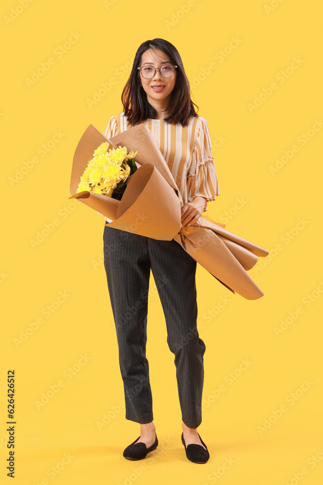 Female Asian teacher with bouquet of flowers on yellow background