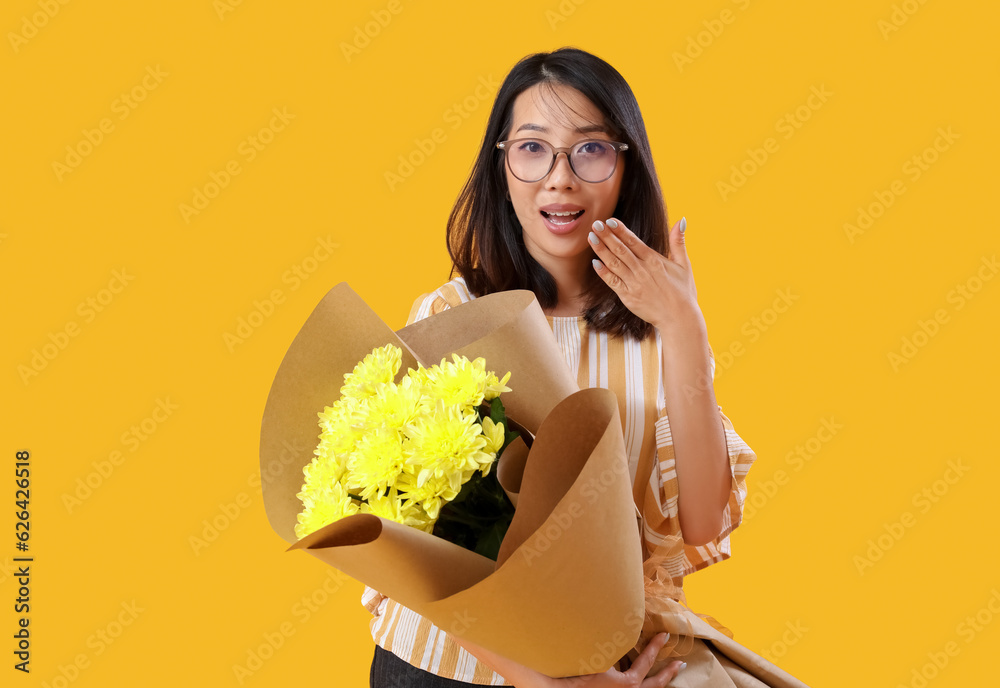 Female Asian teacher with bouquet of flowers on yellow background