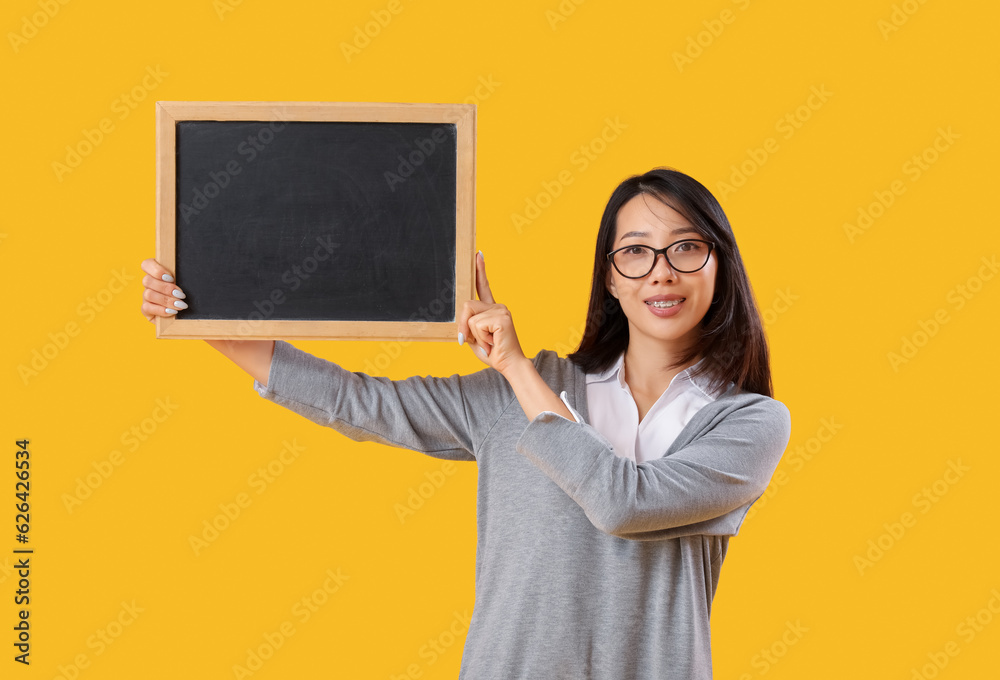 Female Asian teacher with chalkboard on yellow background