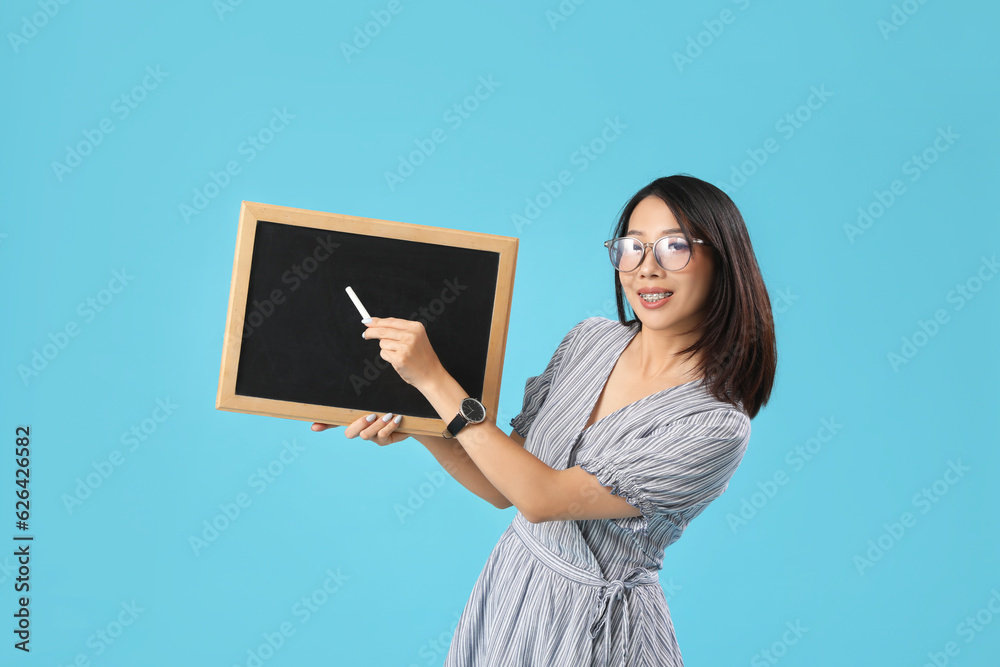 Female Asian teacher with chalkboard on blue background