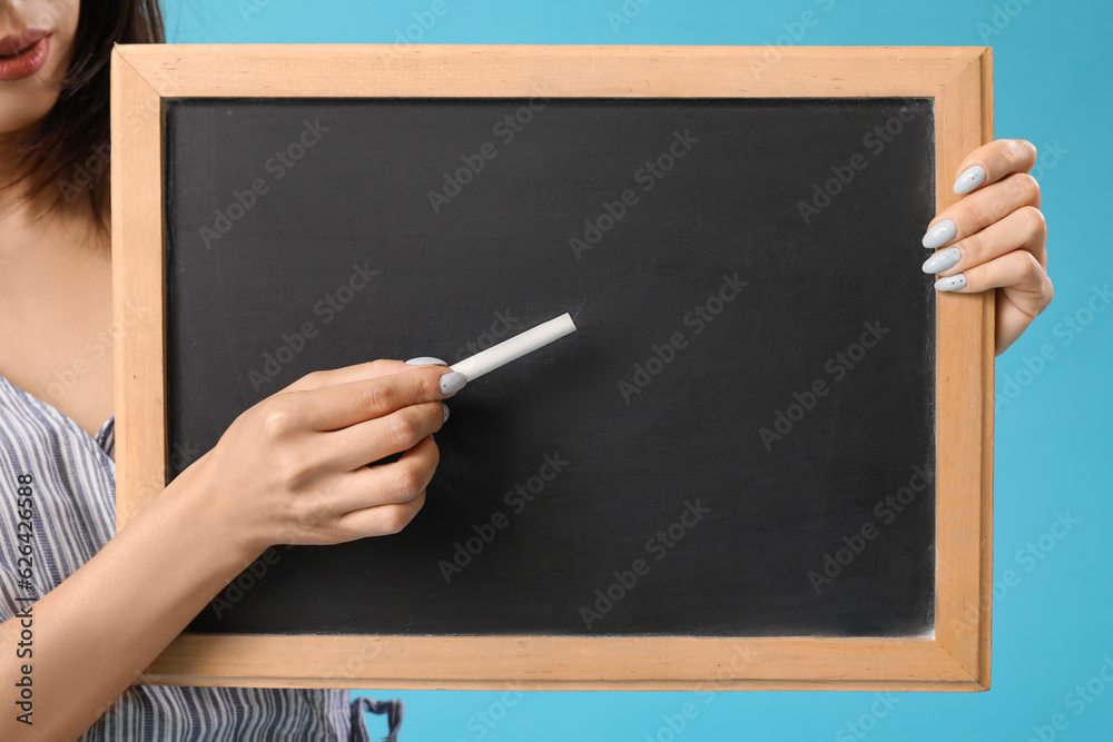 Female Asian teacher with chalkboard on blue background, closeup