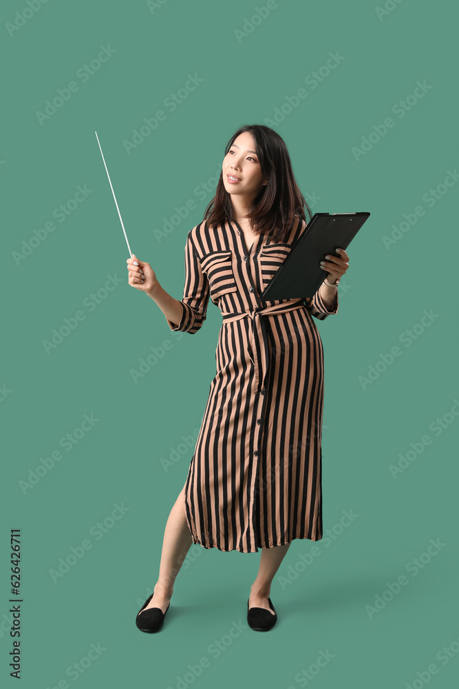 Female Asian teacher with pointer and clipboard on green background