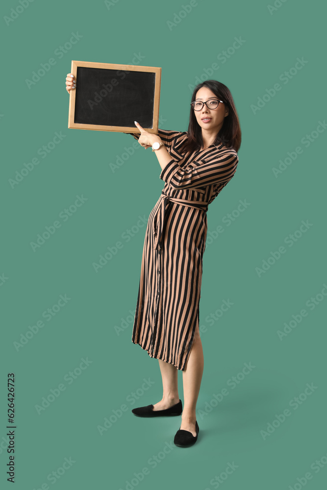 Female Asian teacher pointing at chalkboard on green background