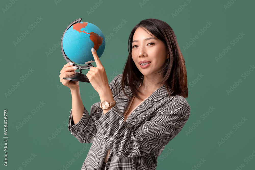 Asian Geography teacher pointing at globe on green background