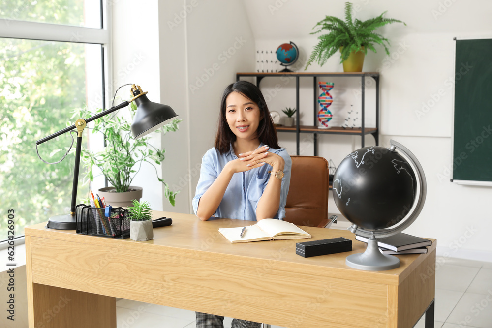 Female Asian teacher sitting at table in classroom