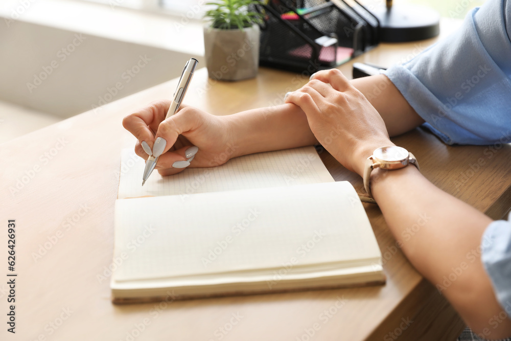 Female Asian teacher writing at table in classroom, closeup