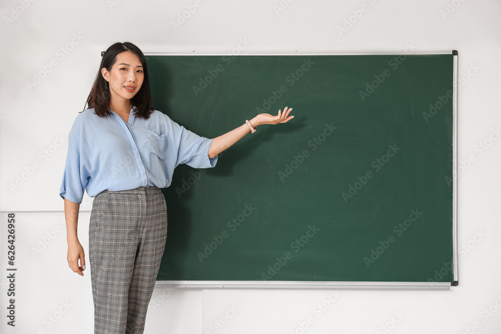 Female Asian teacher near chalkboard in classroom