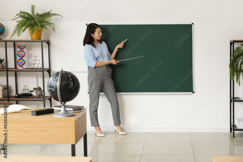 Female Asian teacher near chalkboard in classroom