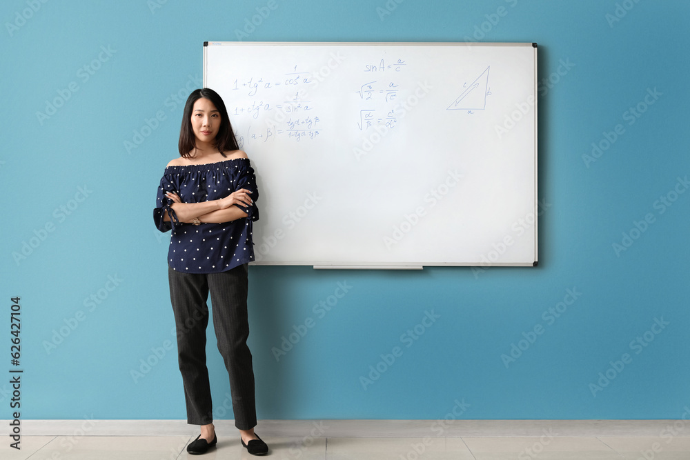 Asian Math teacher near flipboard in classroom