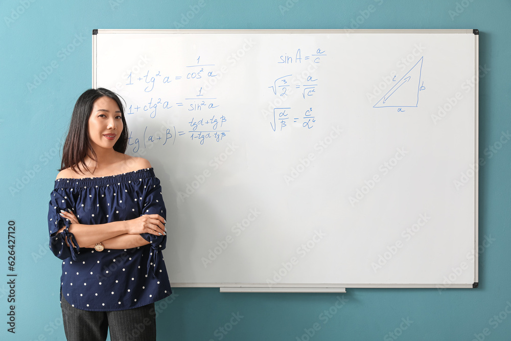 Asian Math teacher near flipboard in classroom