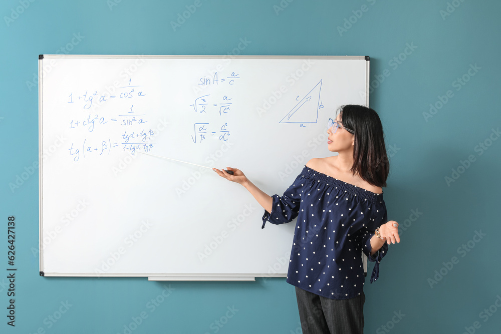 Asian Math teacher near flipboard in classroom