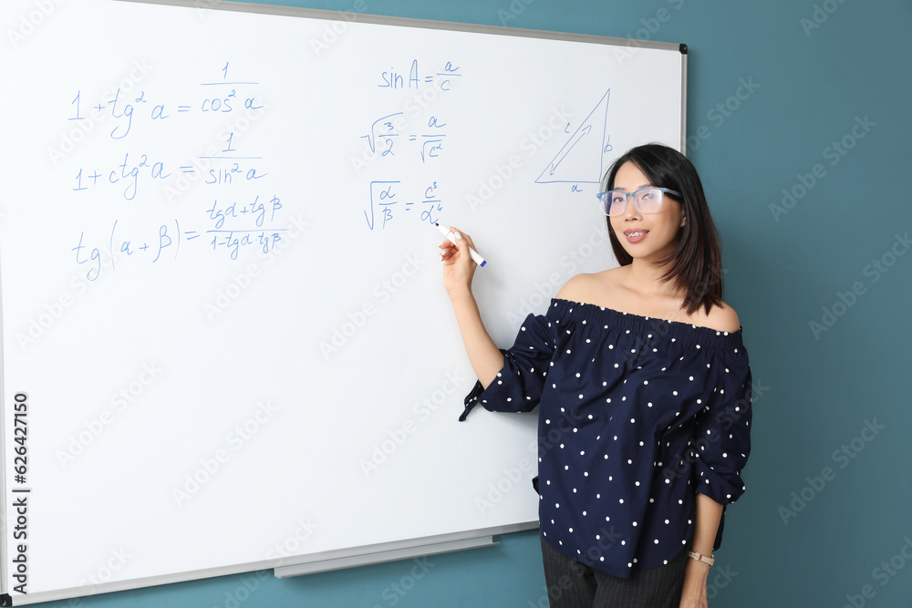 Asian Math teacher near flipboard in classroom