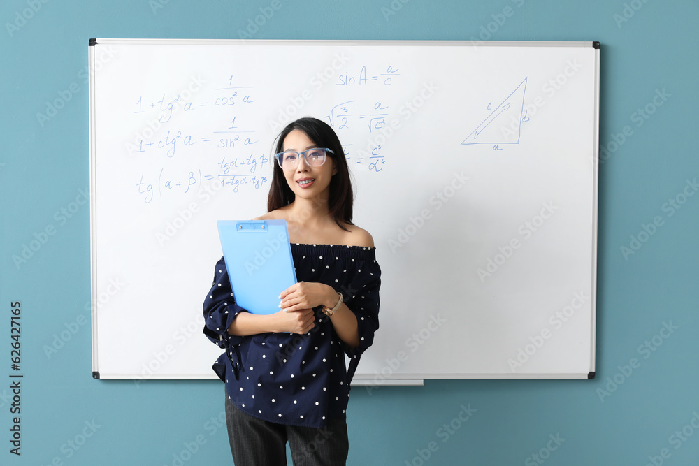 Asian Math teacher with clipboard near flipboard in classroom