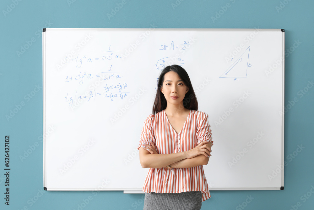 Asian Math teacher near flipboard in classroom