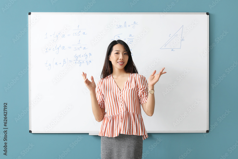 Asian Math teacher near flipboard in classroom