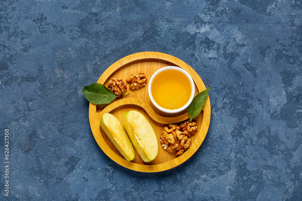 Wooden board with bowl of sweet honey, walnut and apple on blue background