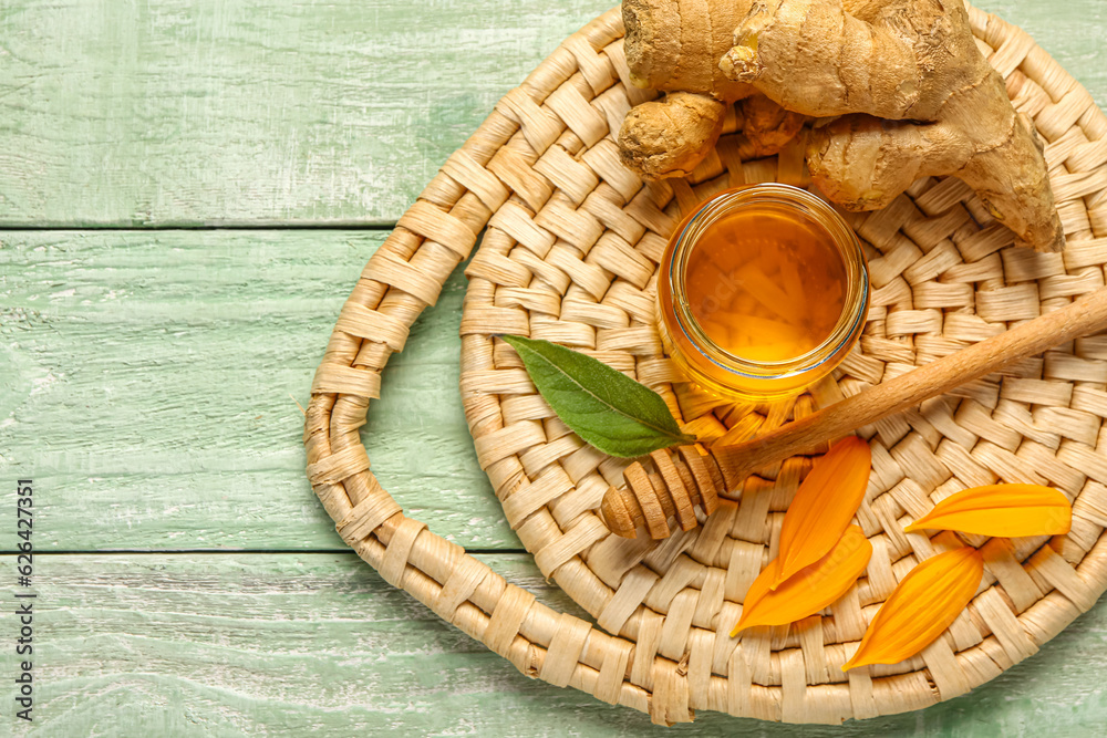 Jar of sweet honey with ginger and petals on green wooden background