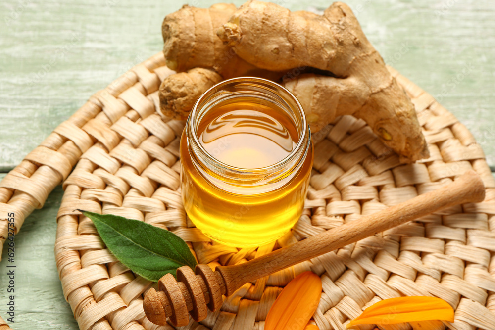 Jar of sweet honey with ginger and petals on green wooden background