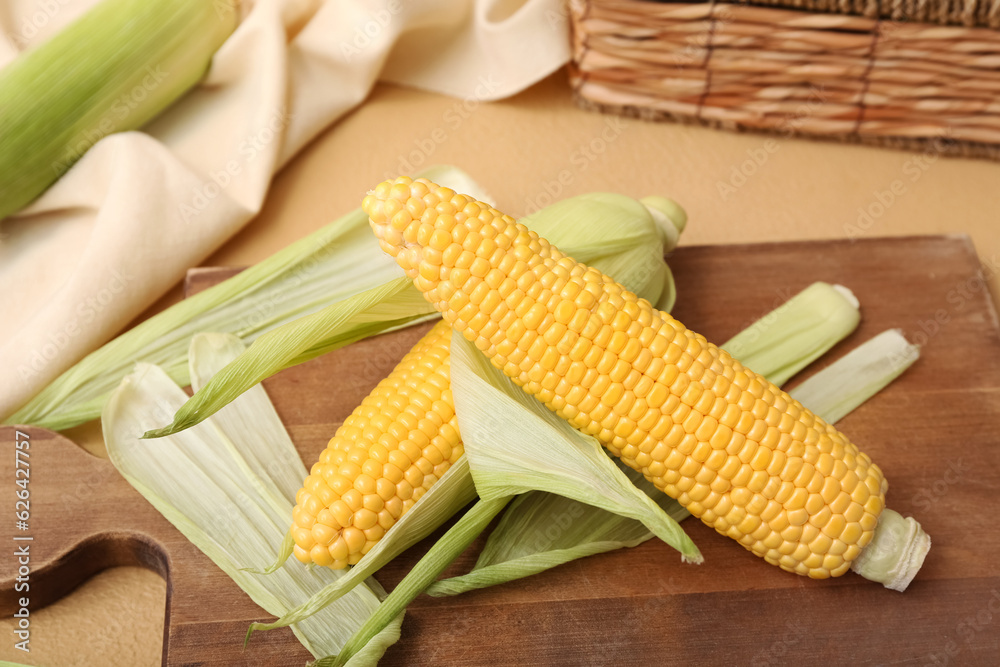 Wooden board with fresh corn cobs on brown background