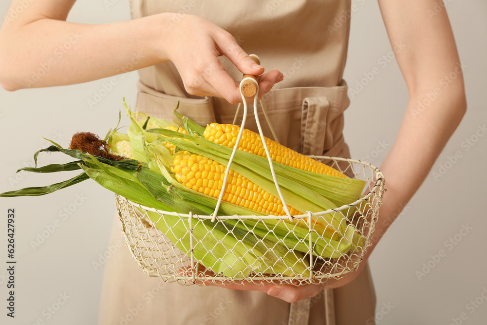 Woman holding basket with fresh corn cobs on white background