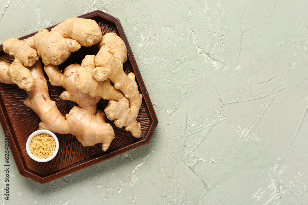 Tray with fresh ginger roots and bowl of dried powder on grey background