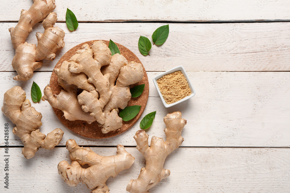 Fresh ginger roots with leaves and bowl of dried powder on white wooden background